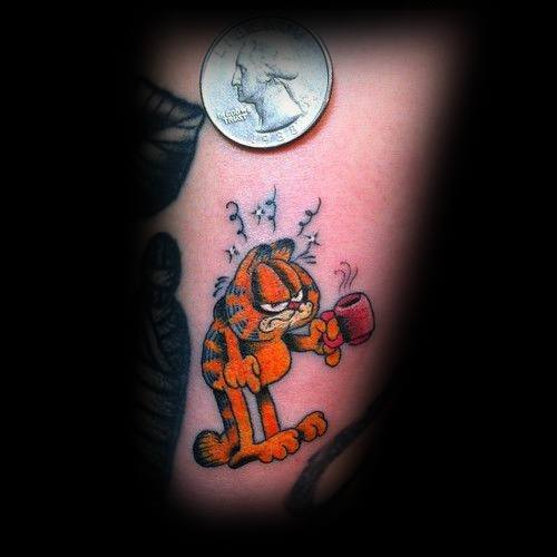 Small Garfield tattoo with a grumpy morning look, holding a coffee cup—perfect for caffeine lovers with a sense of humor.