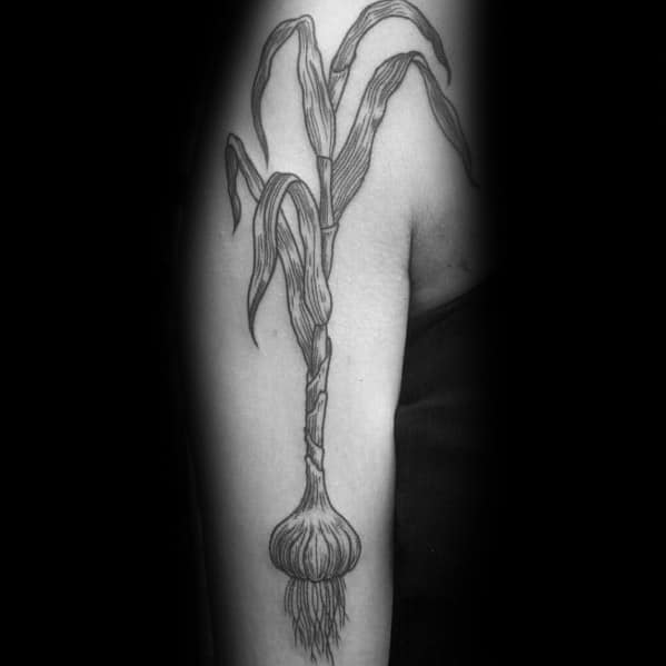 Black and grey garlic tattoo with long, flowing leaves and detailed roots, creating a bold and organic botanical design on the upper arm.