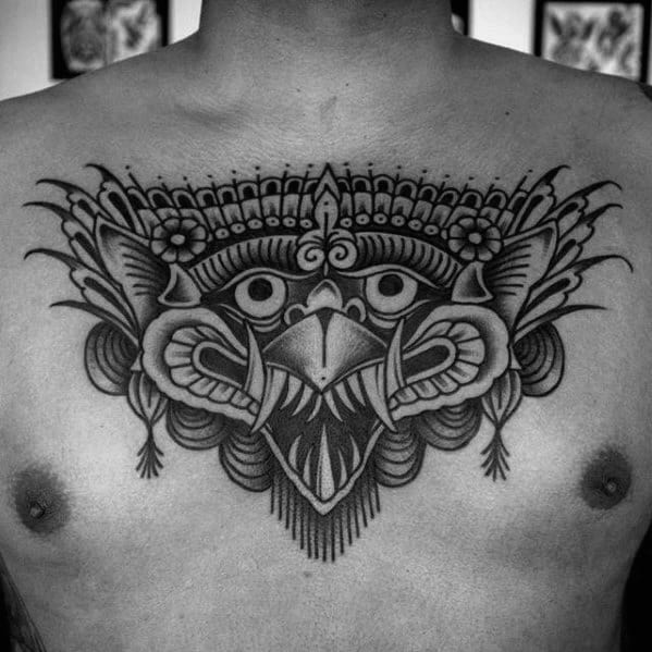 Garuda tattoo design on the chest featuring a symmetrical, stylized bird face with ornate crown and bold black shading.