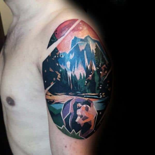 Vibrant geometric landscape tattoo on the upper arm with mountains, forest, lake, and a stylized bear in bold polygonal shapes.