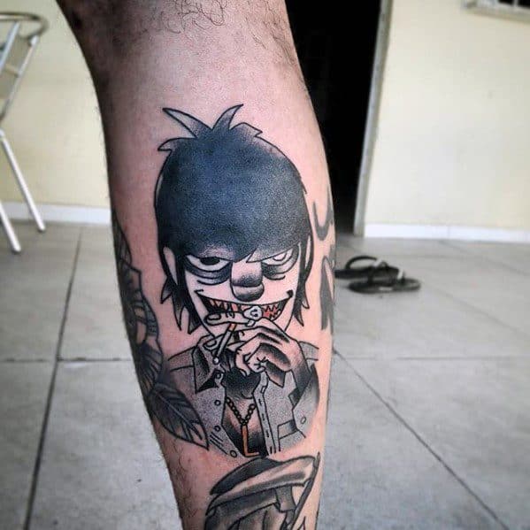 Black and grey tattoo of Murdoc from Gorillaz on the calf, featuring his mischievous grin, necklace, and hand gesture holding a toothpick.