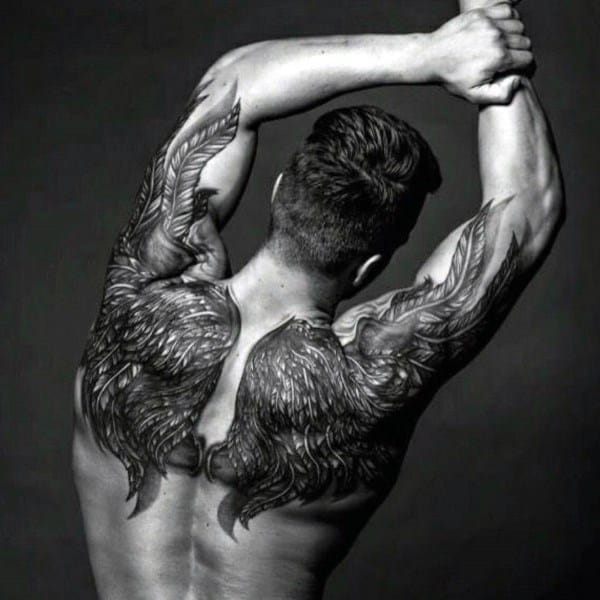 Black and grey tattoo featuring large, detailed angel wings spanning across the upper back and shoulders for a powerful, ethereal look.