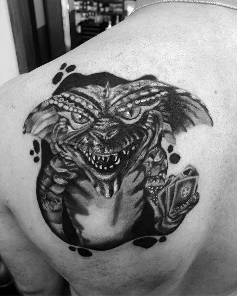Black and gray Gremlin tattoo with fierce details, sharp teeth, and a playing card, creating a bold and menacing design on the back.