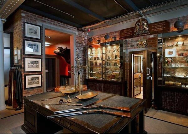 Elegant gun room with exposed brick walls, glass display cases, and a central table showcasing vintage firearms.