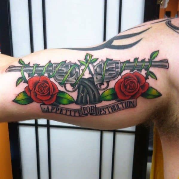 Colorful bicep tattoo with a gun barrel wrapped in barbed wire, red roses, and a banner reading "Appetite for Destruction."