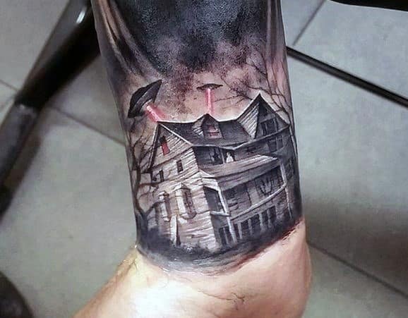 Realistic haunted house tattoo on the leg with two UFOs beaming red lights down, stormy skies, and eerie leafless trees.