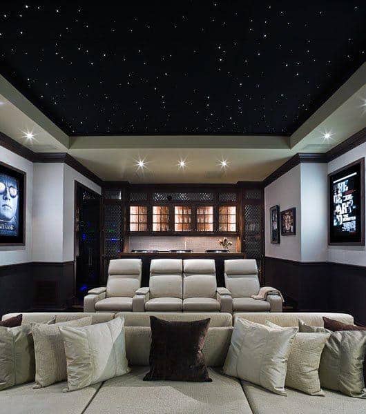 A cozy home theater with white recliners, beige couches, a starry ceiling, and movie posters on the walls