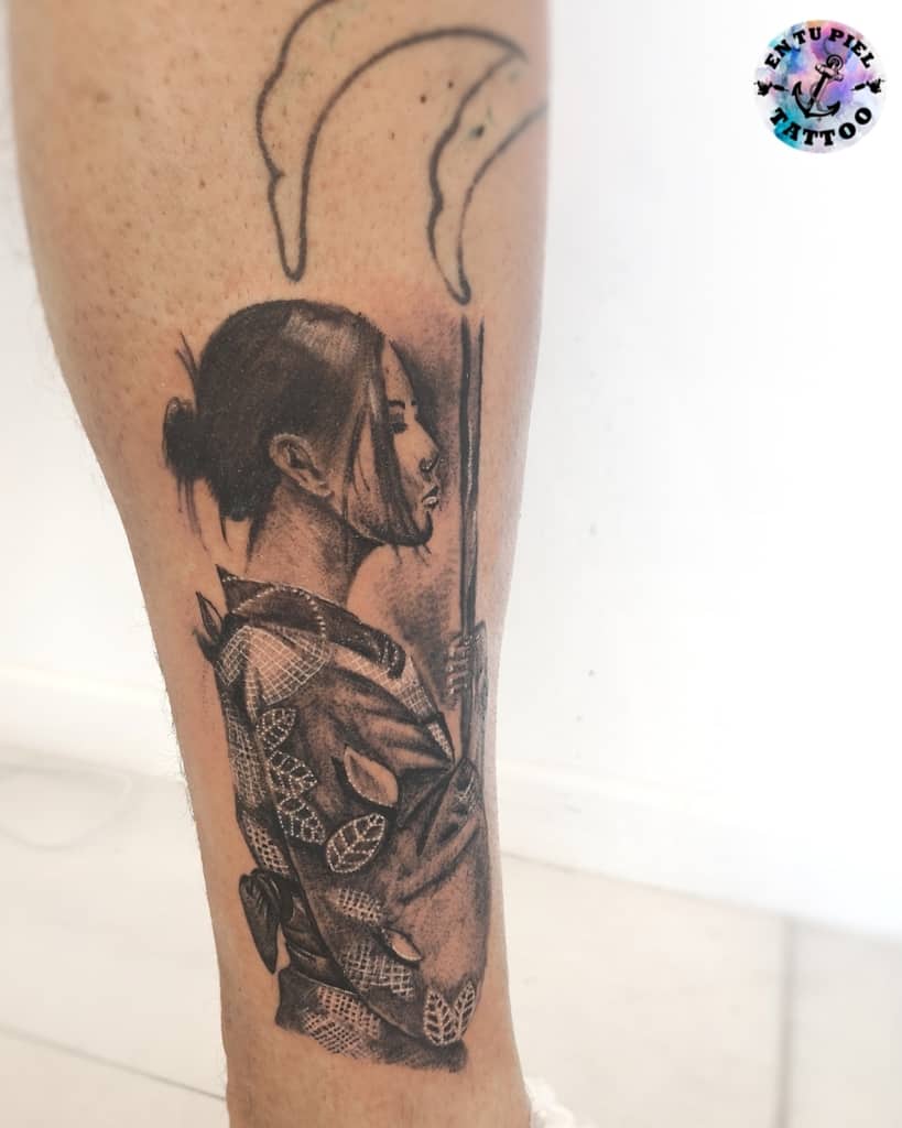 Black and gray tattoo of a woman in a patterned kimono, holding a sword with a calm expression, under two abstract crescent shapes.