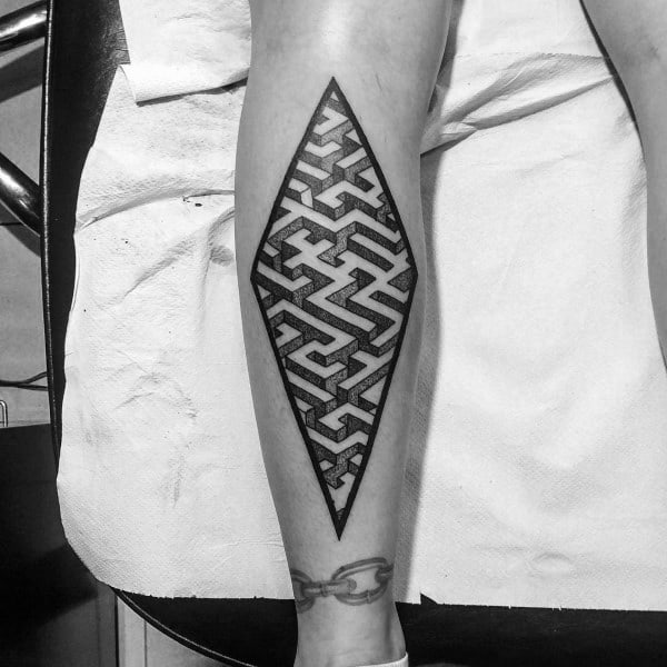 Geometric diamond-shaped labyrinth tattoo on a man's leg, featuring bold black maze patterns enclosed within sharp angular borders.