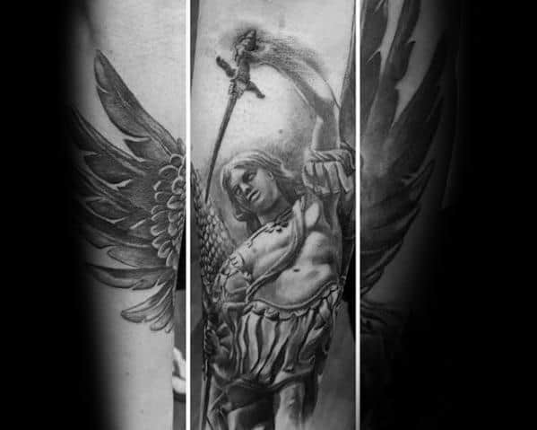 A detailed black and grey full-sleeve tattoo depicting an angel with large wings, holding a sword and standing in a dynamic, powerful pose.