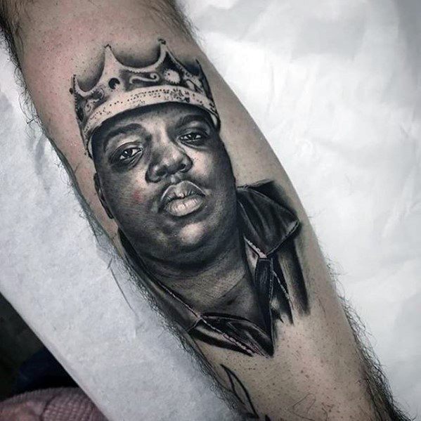 Realistic tattoo of The Notorious B.I.G. wearing a crown, paying tribute to the iconic rapper