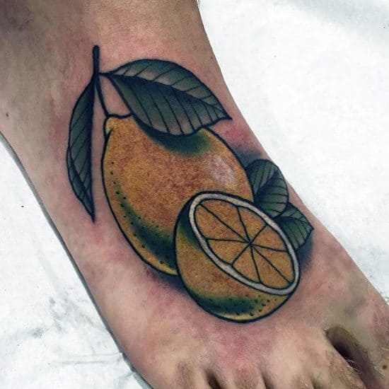 Colorful tattoo of a whole lemon and a lemon slice with bold outlines and green leaves, placed on the top of the foot.