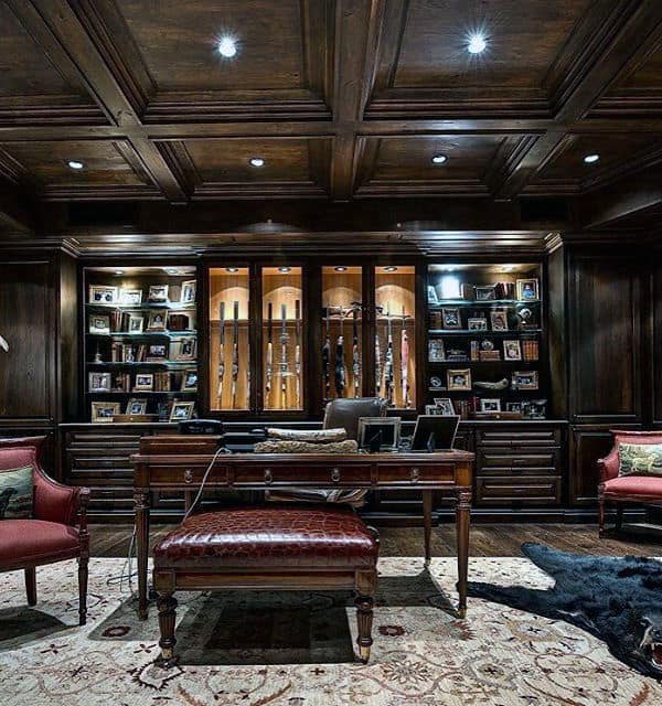 Luxurious gun room with dark wood paneling, built-in illuminated gun cabinets, and a classic office desk for a refined touch.