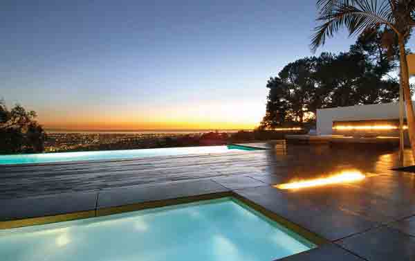 Infinity pool overlooking a city skyline at sunset, with silhouetted trees and a palm tree