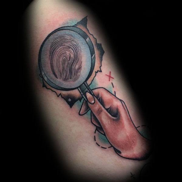 Tattoo of a hand holding a magnifying glass revealing a fingerprint, with a treasure map background, blending mystery and adventure in a colorful design.
