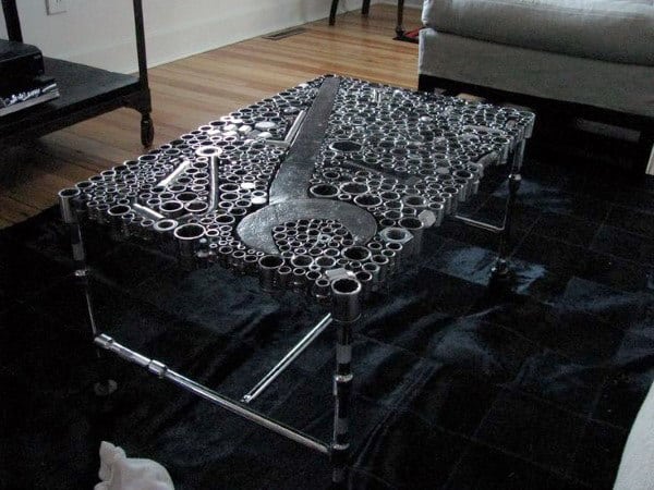 Coffee table made of various metal nuts and bolts, forming intricate patterns on a dark rug