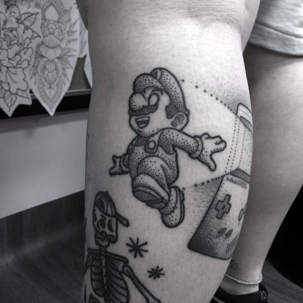 Black and gray dotwork Mario tattoo featuring a retro gaming theme, with pixel-inspired shading and a nostalgic Game Boy design in the background.