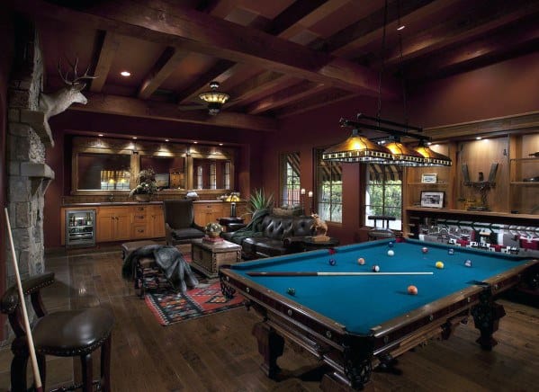 Rustic billiard room with exposed beams, leather seating, and a bar area with warm lighting.