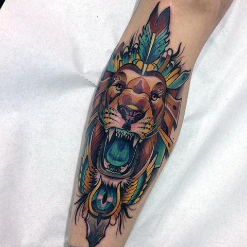 Neo-traditional lion tattoo on forearm with tribal feathers, bold teal accents, and a roaring expression for a fierce, artistic vibe.
