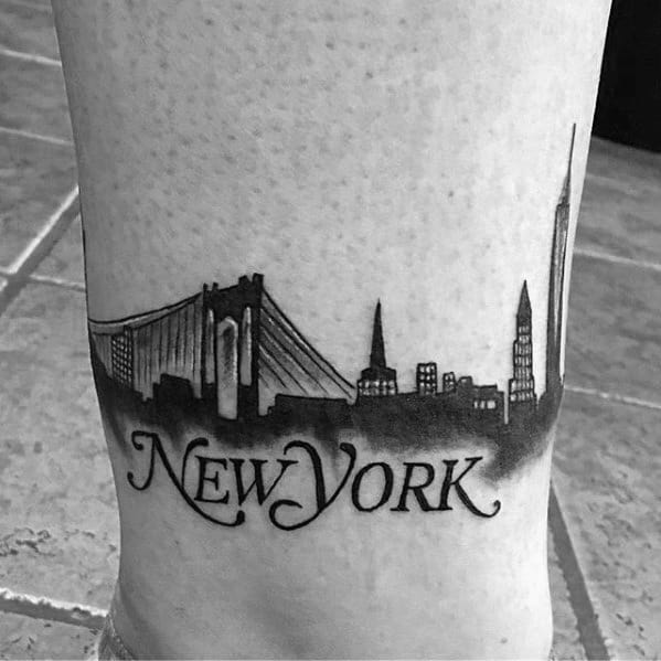 Black ink tattoo of the New York City skyline with the Brooklyn Bridge and "New York" written below in elegant script.