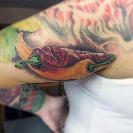 Realistic chili pepper tattoo on the upper arm, featuring a red and yellow pepper with rich shading and texture for a bold, vibrant look.