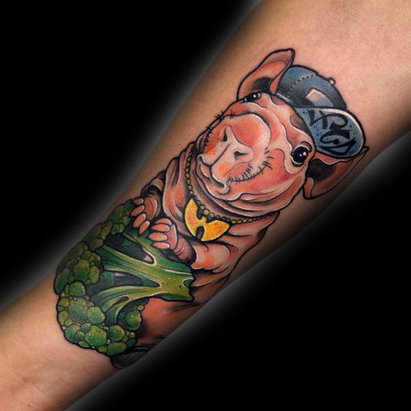 Hyper-realistic tattoo of a guinea pig wearing a cap and chain, holding a broccoli, featuring vibrant colors and bold shading for a playful design.