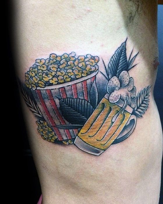 Tattoo of a popcorn bucket and frothy beer mug with green leaves, blending food, drink, and botanical elements in a bold style.
