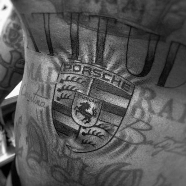 Large grayscale Porsche emblem tattoo across the chest, accented by stylized rays and detailed shading.
