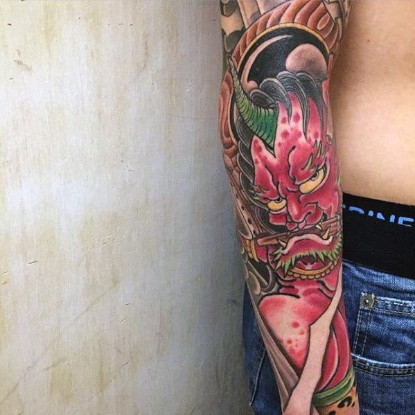 Vivid Raijin lower sleeve tattoo with intense red face, green horns, and fierce expression in bold traditional Japanese style.