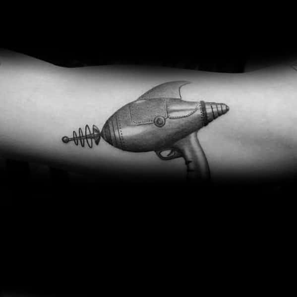 Black and grey ray gun tattoo with a sleek retro-futuristic design, featuring fine shading, smooth metallic details, and a classic sci-fi aesthetic.