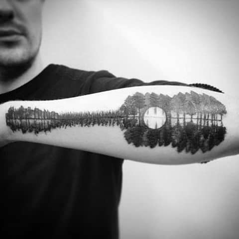 Tattoo of a forest and full moon reflected on a calm lake, creating a symmetrical and serene nature-inspired design along the forearm.