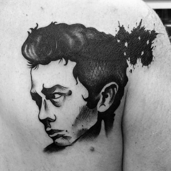 Stylized black ink tattoo of James Dean’s side profile with bold shading and an abstract splatter effect behind his head.