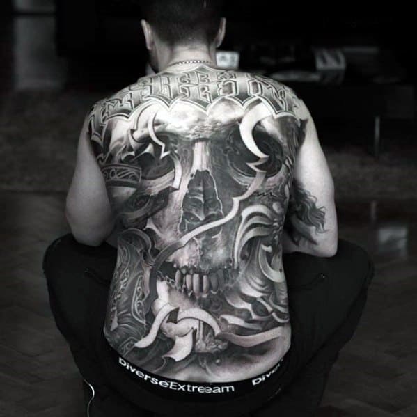Full back skull tattoo with swirling abstract shapes, tribal influences, and bold “Freedom” lettering across the upper shoulders.