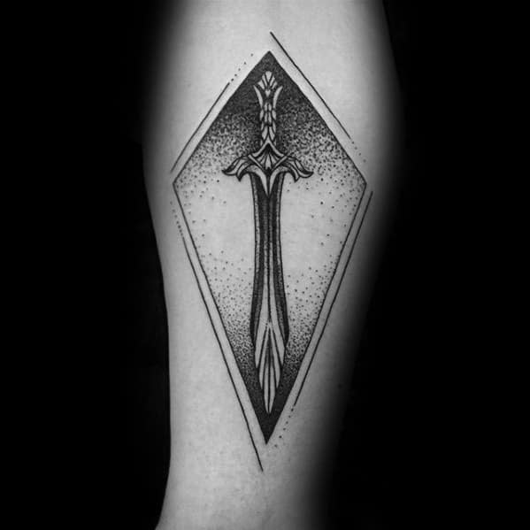 Skyrim-themed tattoo of a detailed sword inside a diamond shape on an arm