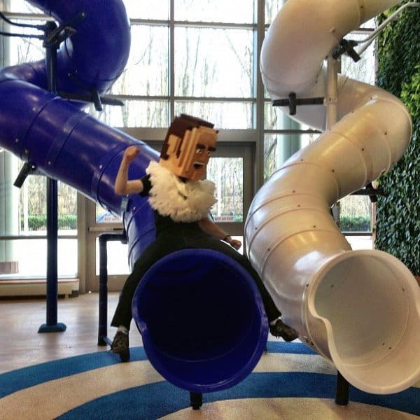 Person with a pixelated mask swiftly sliding down a giant blue slide indoors