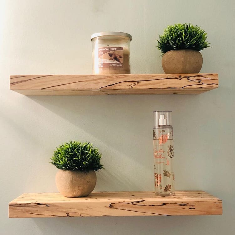 Simple wooden floating shelves with small potted plants, candle, and body spray.