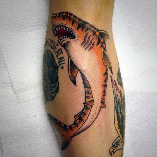 Curved tiger shark tattoo in bold traditional style with orange and black tones, open jaws, and a fierce vintage-inspired design.