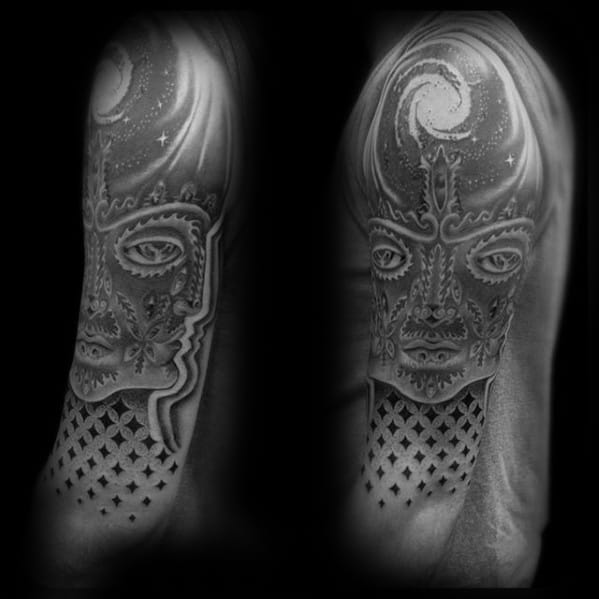 Black and grey Tool-inspired upper arm tattoo of a cosmic-faced figure with ornate patterns, glowing eyes, and a swirling galaxy above.