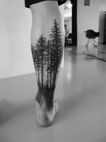 Black ink forest tattoo on the leg, featuring tall pine trees fading into the skin, creating a realistic and immersive nature-inspired design.