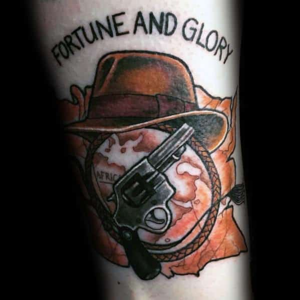 Indiana Jones tattoo featuring his fedora, whip, revolver, and a map of Africa, with 'Fortune and Glory' inscribed above.