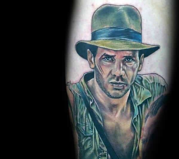 Realistic Indiana Jones tattoo featuring his intense expression, iconic fedora, and rugged adventure outfit with detailed shading.