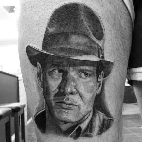 Black and gray Indiana Jones tattoo featuring a realistic portrait with his iconic fedora and a determined expression.