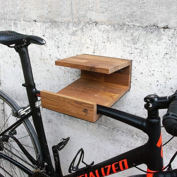 Bicycle mounted on a modern wooden wall rack with a built-in shelf for indoor storage.