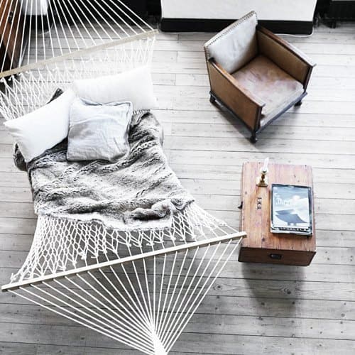 White hammock with soft pillows and a blanket in a rustic room with a chair and wooden table.