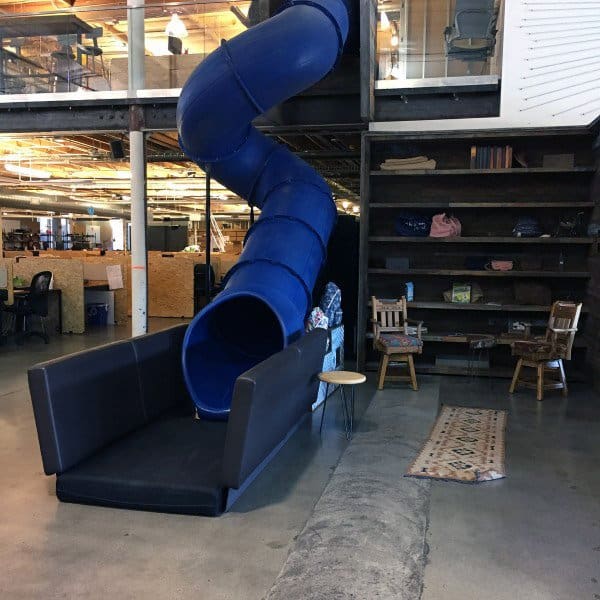 Office space featuring a blue slide, comfy seating area, and stylish bookshelves