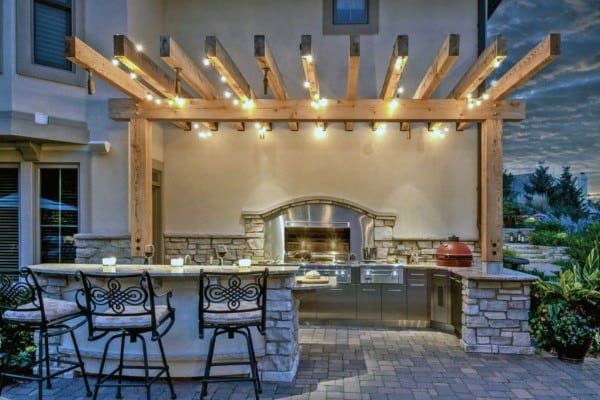 Outdoor kitchen featuring a stone bar, grill, and pergola with string lights at dusk