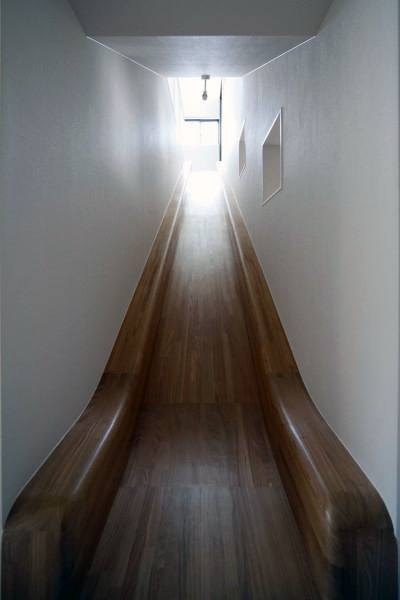 A smooth wooden slide glides through a narrow, white-walled corridor to a bright window