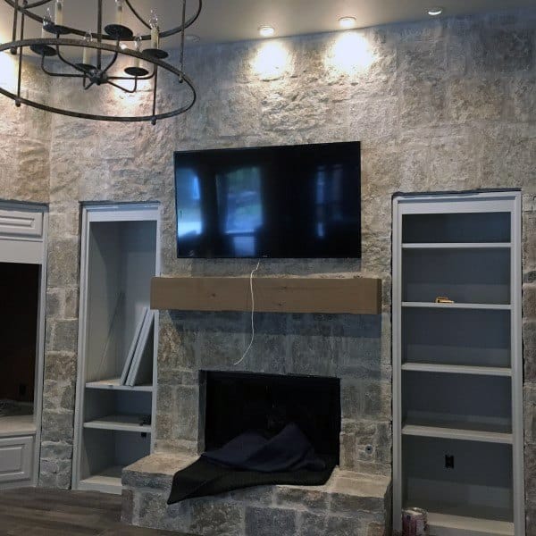 Modern living room with stone fireplace, wooden mantel, built-in shelving, and mounted TV.