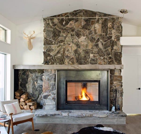 Modern living room with large stone fireplace, metal surround, and stacked firewood storage.