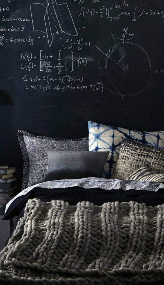 Bed with gray knitted blanket, pillows, and chalkboard wall with mathematical equations